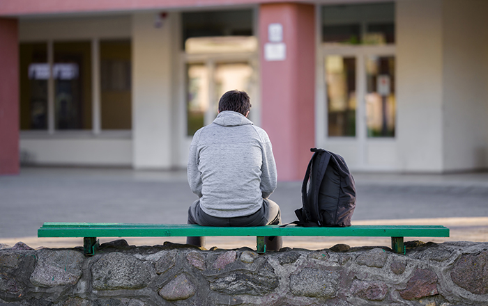 A photo of a university student sitting on a bench. 
